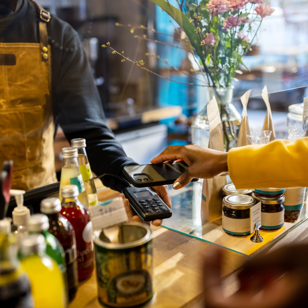 Cropped shot of a female customer using a smartphone for contactless payment. Cafe owner and customer at the checkout counter in a coffee shop.